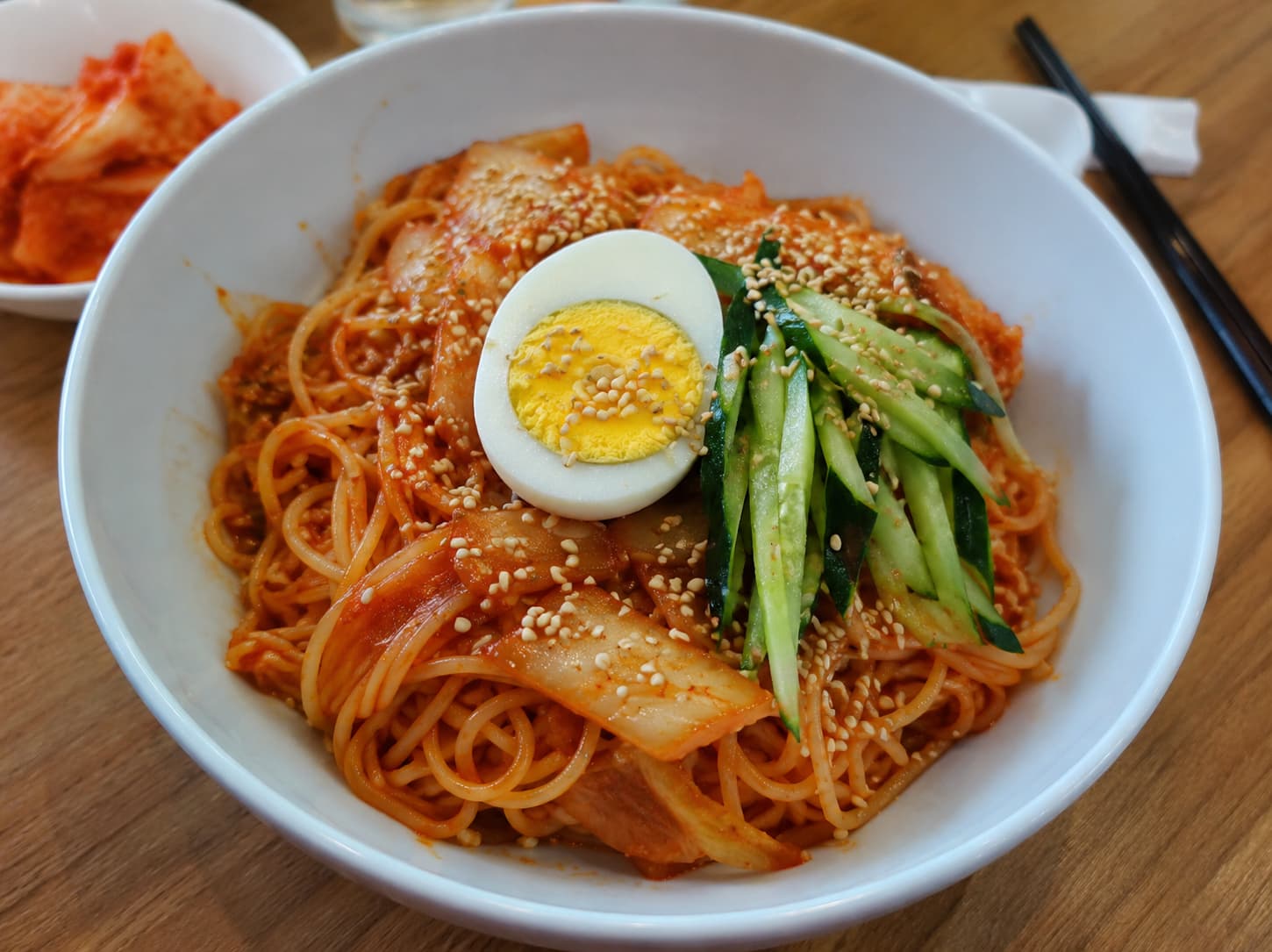 Bowl of spicy cold kimchi noodles topped with cucumber and egg
