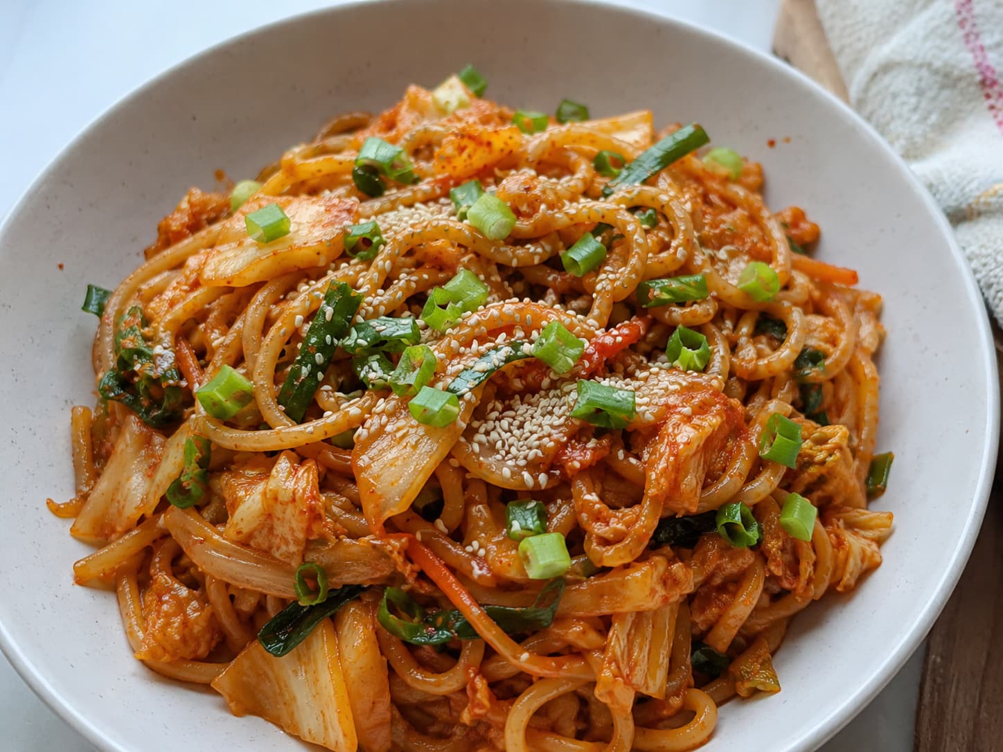 Kimchi udon stir fry with bacon, egg, and green onion in a black bowl