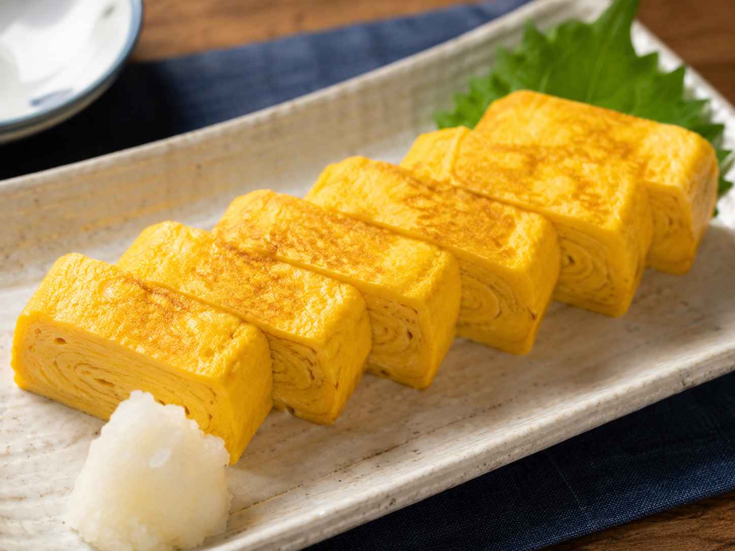 Sliced tamagoyaki Japanese rolled omelette showing golden egg layers, served with grated daikon